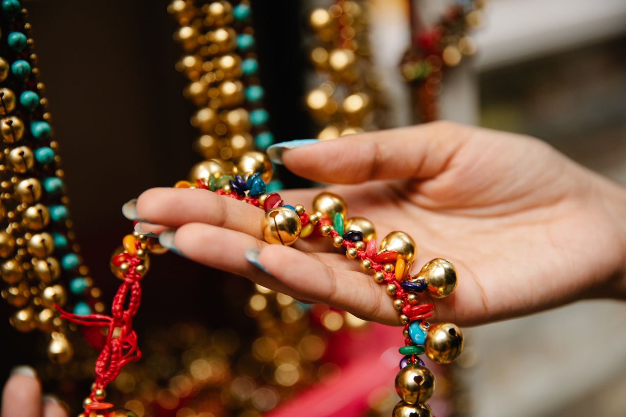 Hand holding a vibrant beaded necklace with golden, red, and turquoise elements.